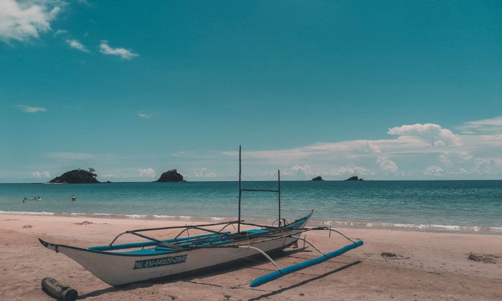 A traditional outrigger boat on the sand at El Nido, Palawan, with small islands on the horizon