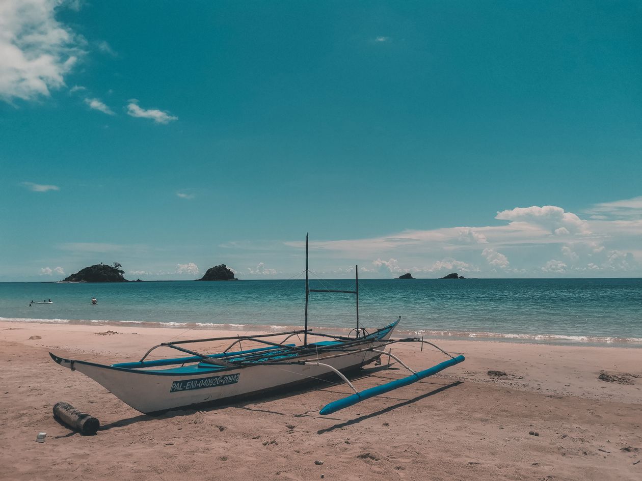 A traditional outrigger boat on the sand at El Nido, Palawan, with small islands on the horizon