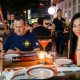 A man looking at his phone and a woman looking at the camera while seated have dinner outdoors in the Philippines.