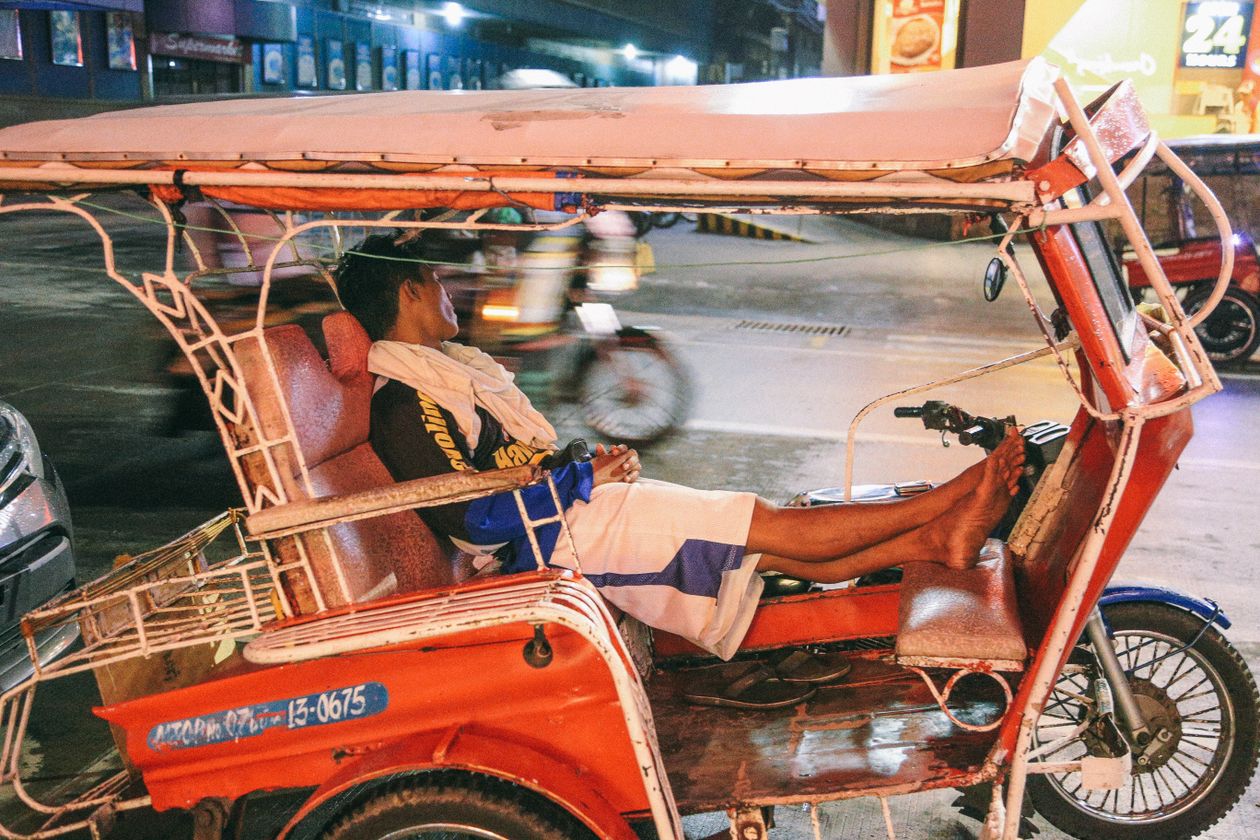 A tricycle driver waiting in his red tricycle at night on a street in Dumaguete, Philippines.