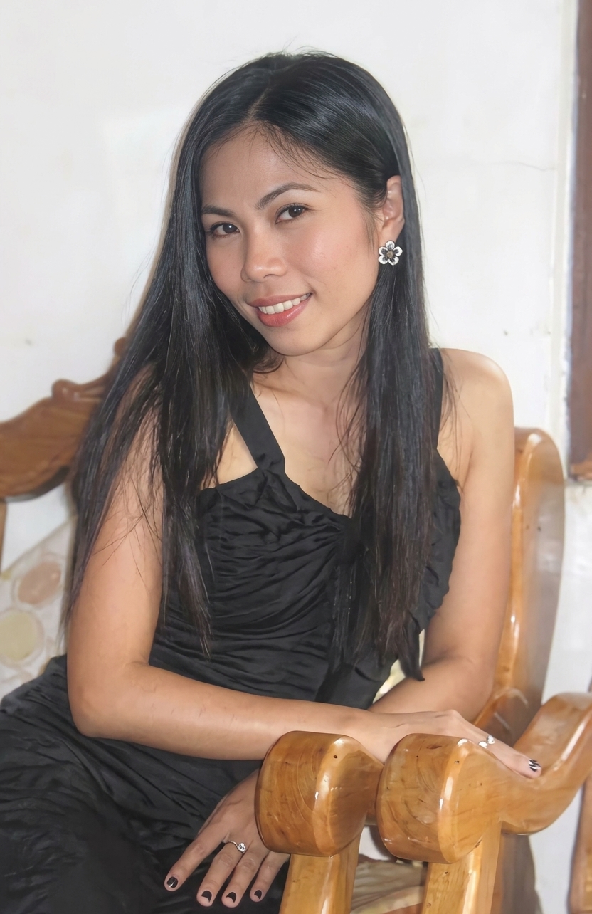 A beautiful Filipina woman sitting in a wooden chair wearing a black dress.
