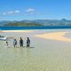 A small group of 4 people walking through shallow water on a sandbar with mountains in the background on a sunny day at the Manjuyod Sandbar, a day trip from Dumaguete, Philippines.