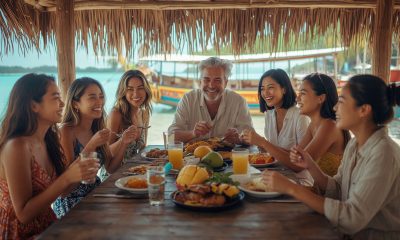 Group of friends sharing a Filipino meal at a beachside eatery with a traditional bangka boat and turquoise water in the background in the Philippines.