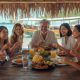 Group of friends sharing a Filipino meal at a beachside eatery with a traditional bangka boat and turquoise water in the background in the Philippines.